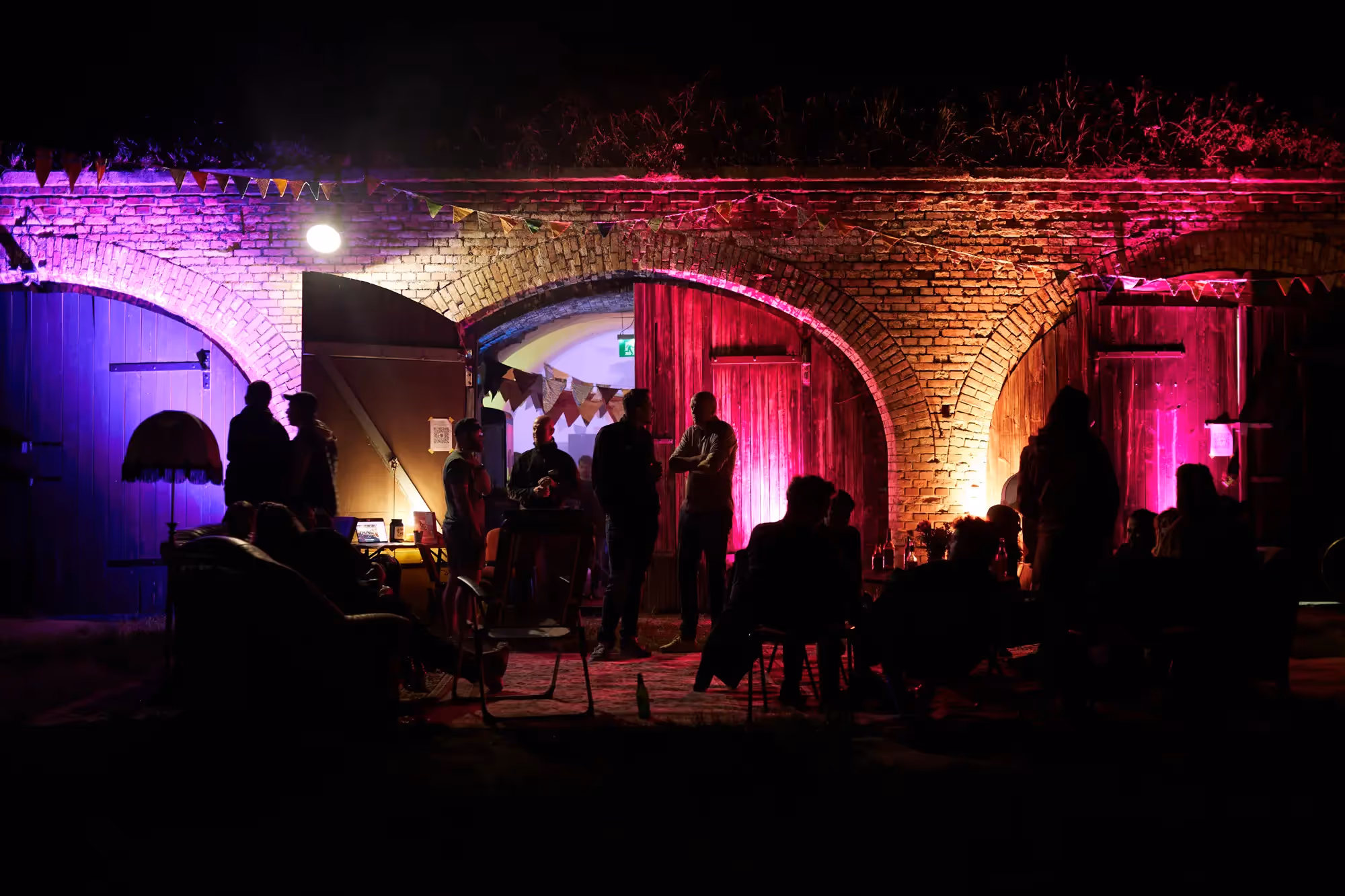 People stand in front of an illuminated tent stage in the dark.