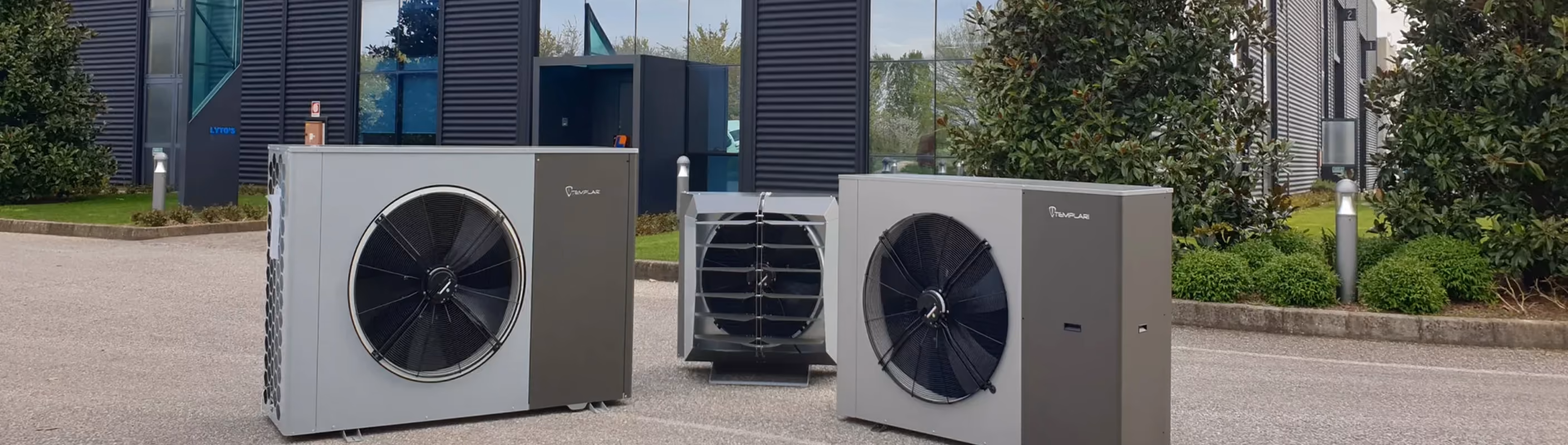 Drie warmtepomp-buitenunits opgesteld op een bedrijventerrein voor een modern kantoorpand met donkere gevel