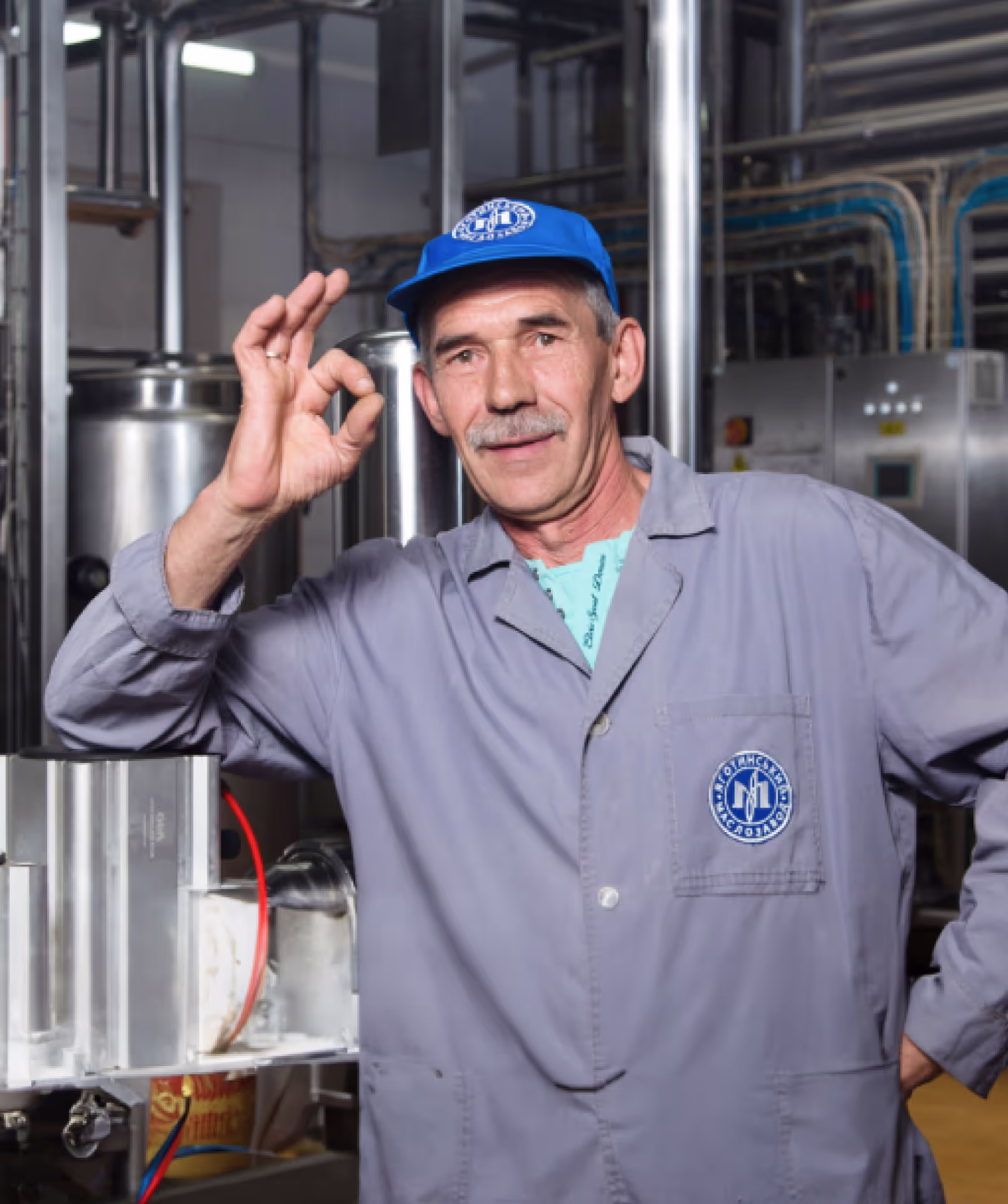 A smiling dairy factory worker wearing a blue cap and gray uniform with a company logo