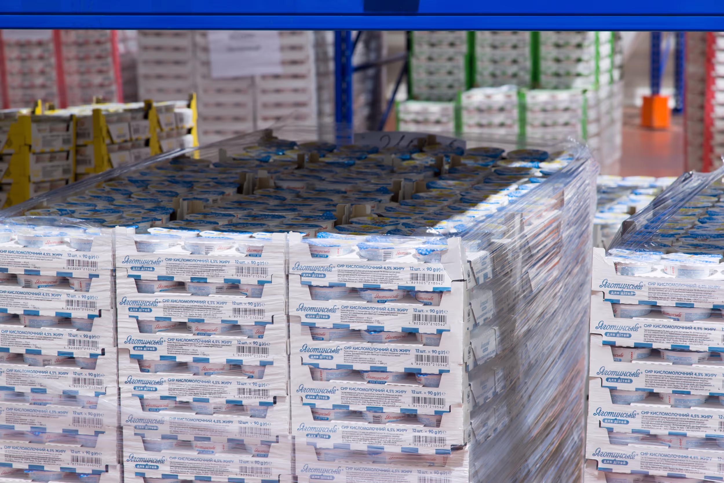 Large pallet of ‘Яготинське для дітей’ (Yahotynske for Children) dairy products wrapped in plastic film, ready for distribution. The packaging contains multiple packs of cottage cheese with 4.5% fat content, stacked in a warehouse setting.