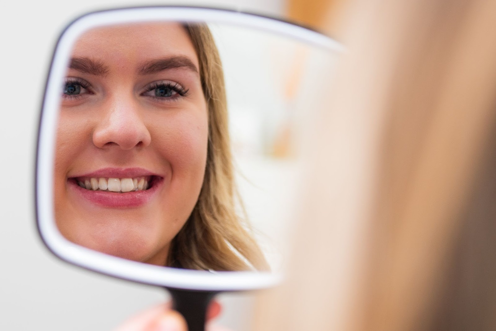 Woman checking her brightened smile in a mirror after professional teeth whitening in Croydon