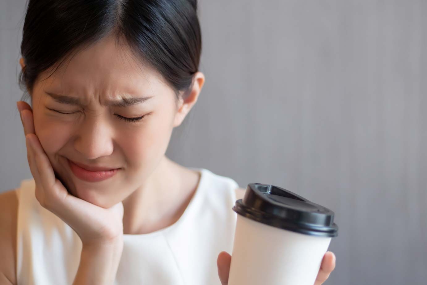 Woman holding her cheek in pain with coffee cup, illustrating sudden toothache and need for emergency dentist in Croydon