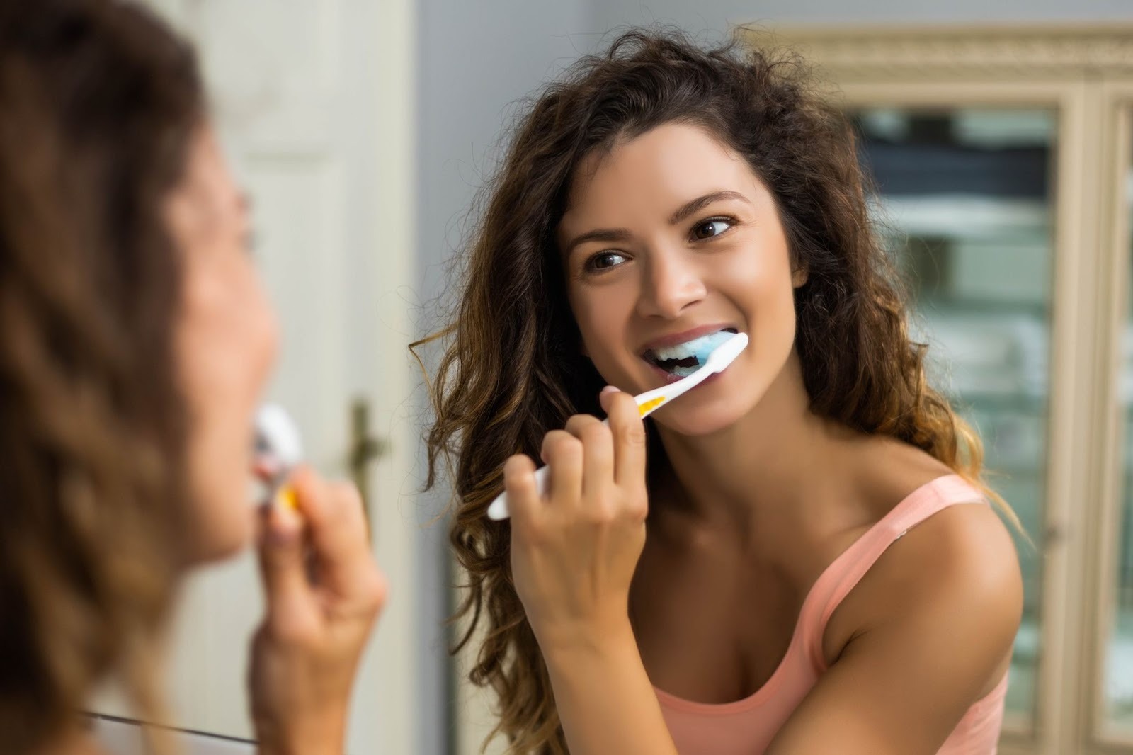 Woman brushing her teeth at home to maintain healthy teeth and cosmetic dental treatments