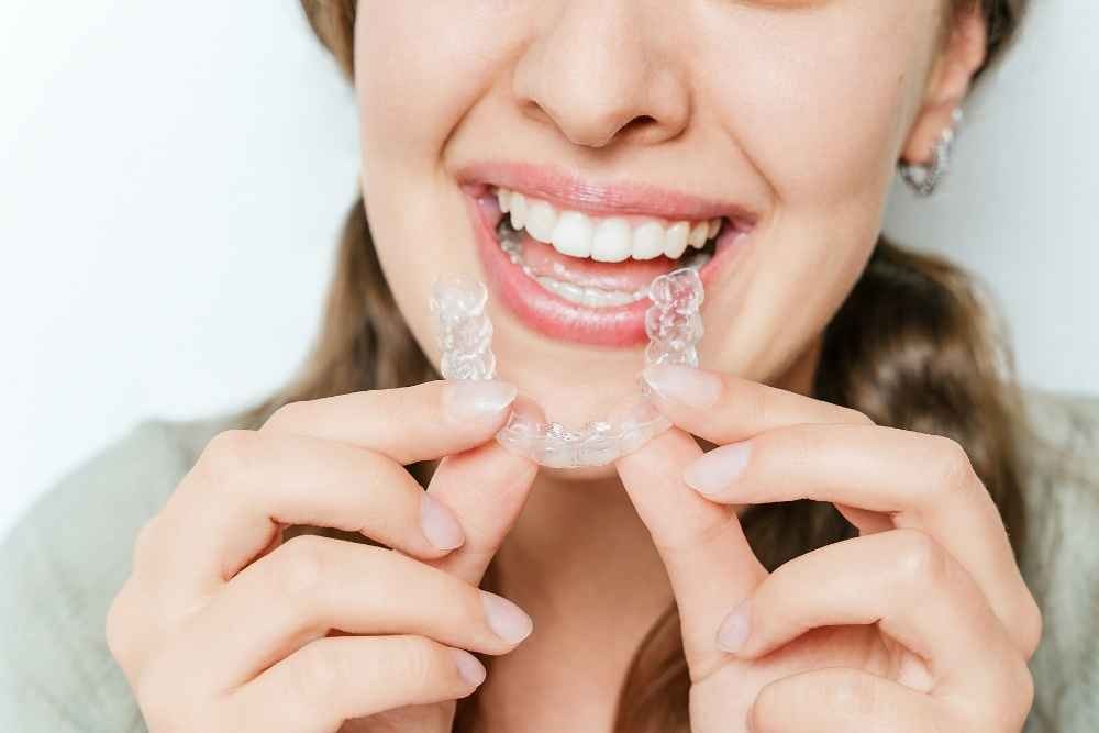 Woman putting clear Invisalign aligners over her teeth