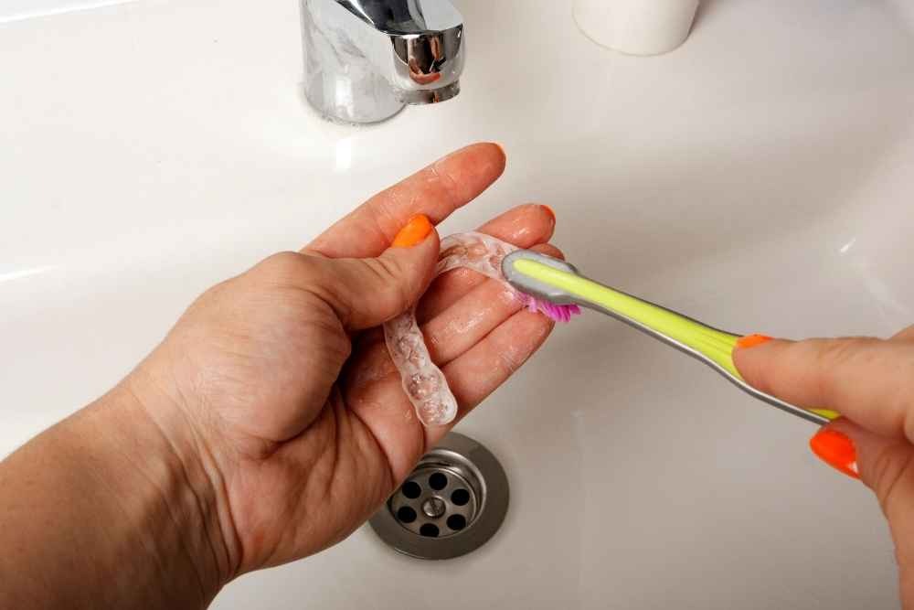 Clear dental aligner being cleaned with a toothbrush