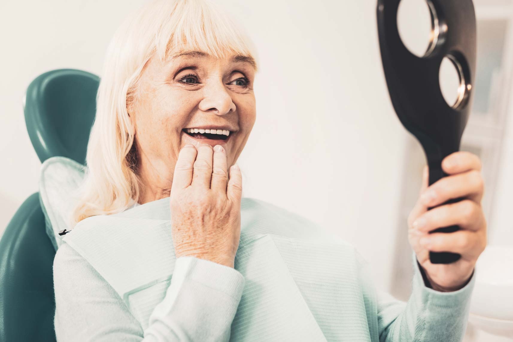 Older patient smiling and checking teeth in mirror after restorative dental treatment at a Purley dental clinic