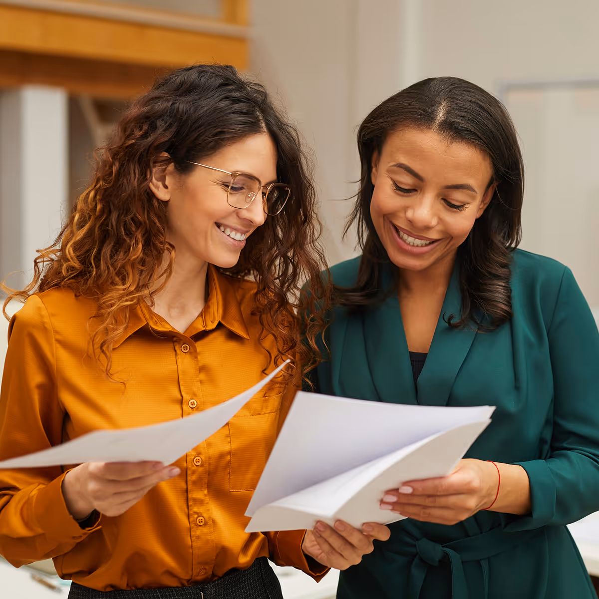Two women smiling and reviewing documents together in a professional setting—representing accessible, collaborative HR resources.
