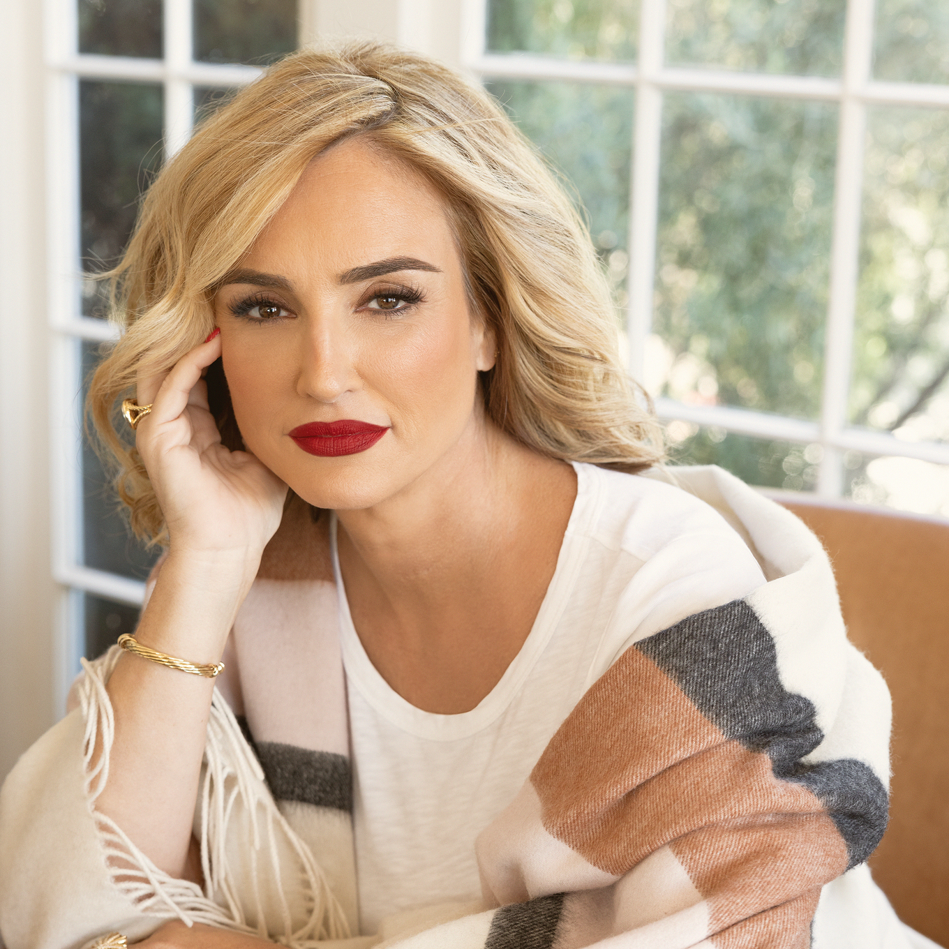Michele Locke with red lipstick and a striped shawl looking thoughtfully at the camera indoors.
