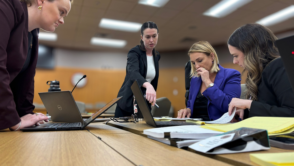 Two women in a meeting room collaborating over laptops and documents on a wooden table.