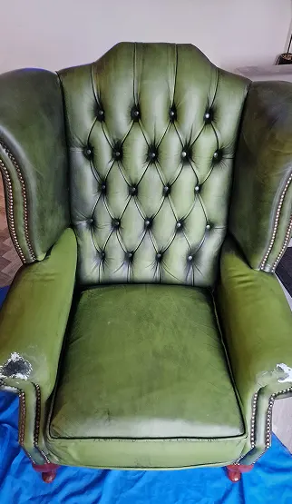 Green upholstered armchair with button-tufted backrest, showing wear and damage on the armrests.