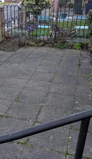Sloped outdoor area with stone tiles and metal railing leading to a fenced garden with plants and benches.