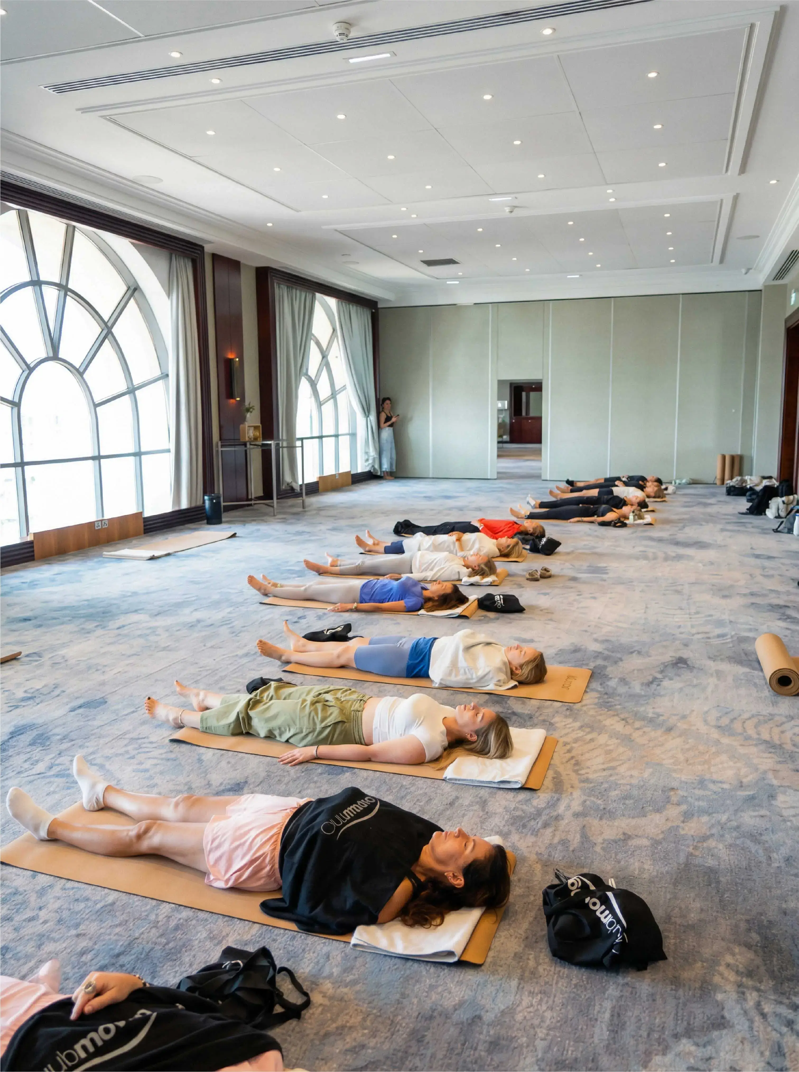 Un groupe de personnes allongées sur des tapis de yoga dans une grande salle lumineuse.