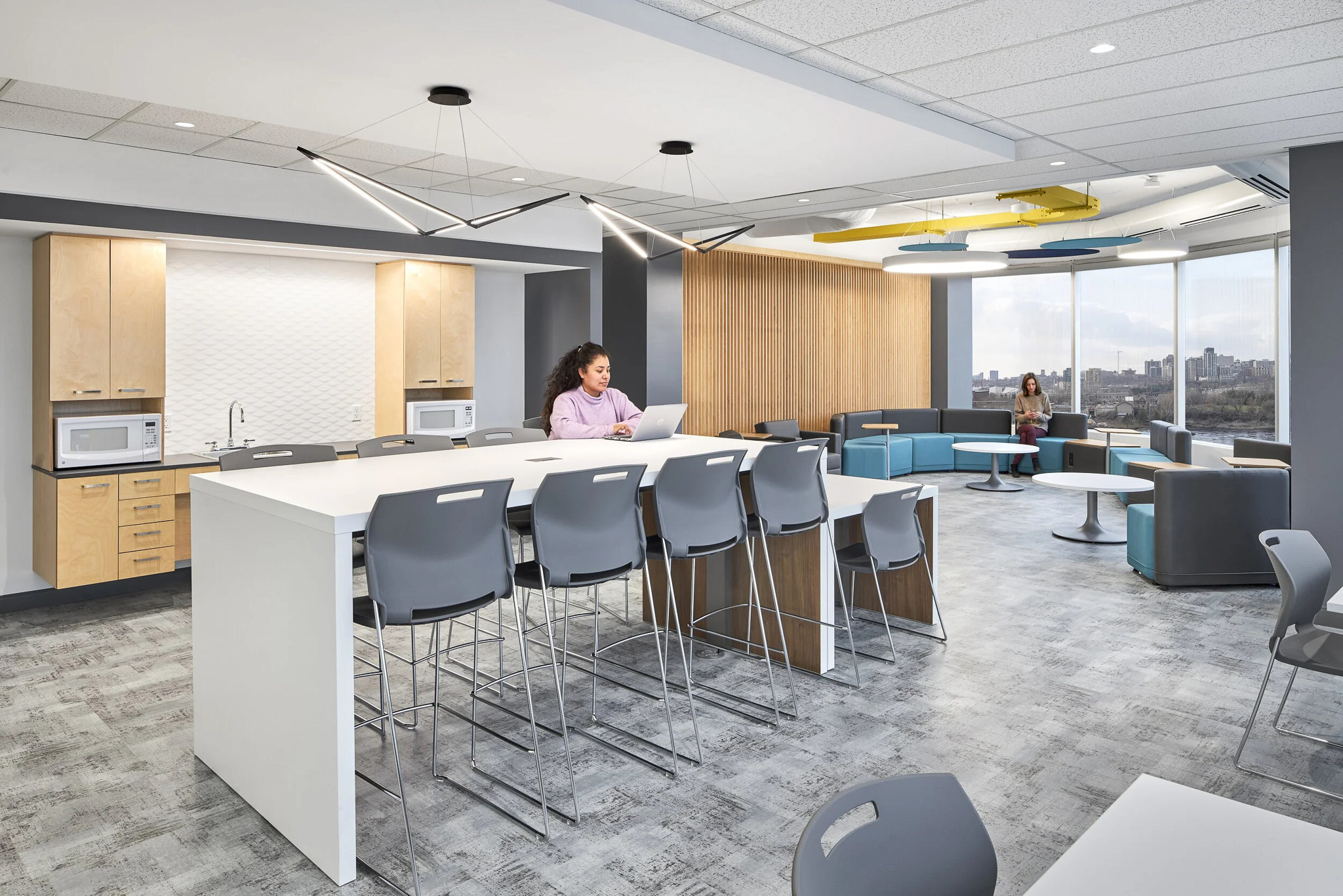 Modern interior office space featuring neutral whites and grays with blue and yellow accents. Various seating arrangements available. 