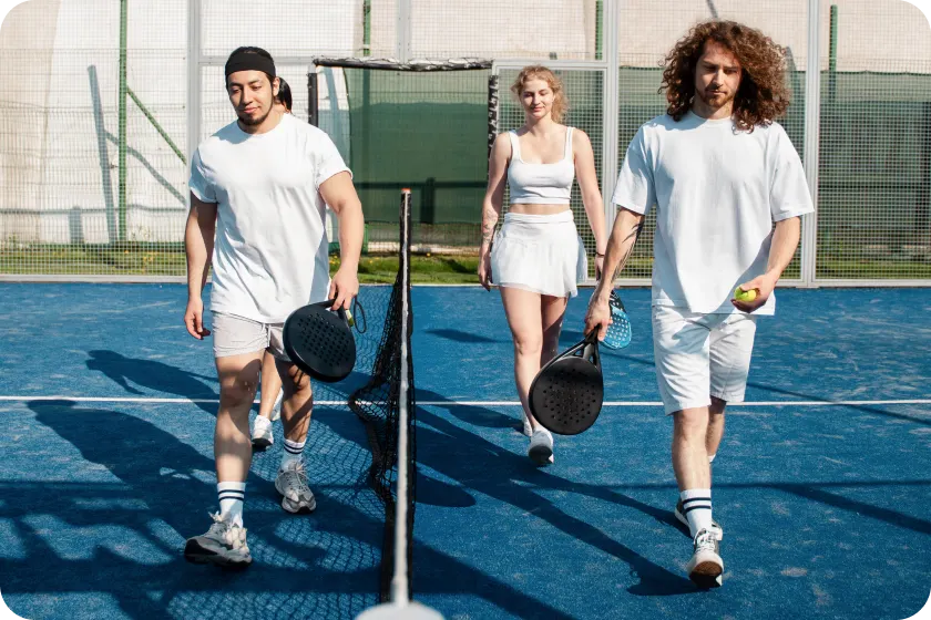 4 joueurs et joueuses de padel habillés en blanc sur un terrain de padel en extérieur.