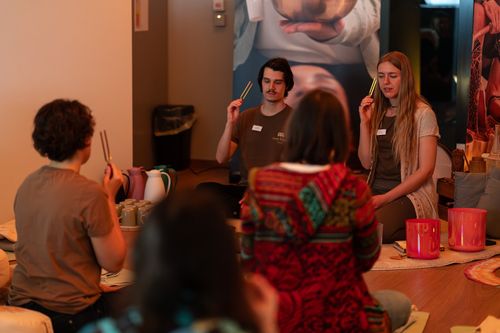 Gruppe sitzt auf dem Boden bei Klangschalen-Meditation, hält Stimmgabeln in Händen.