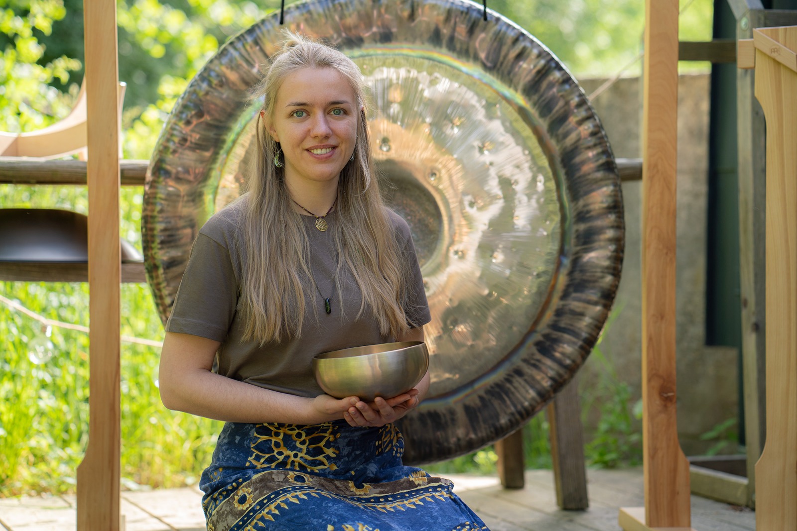 Junge Frau sitzt vor einem großen Gong und hält eine Klangschale in den Händen.