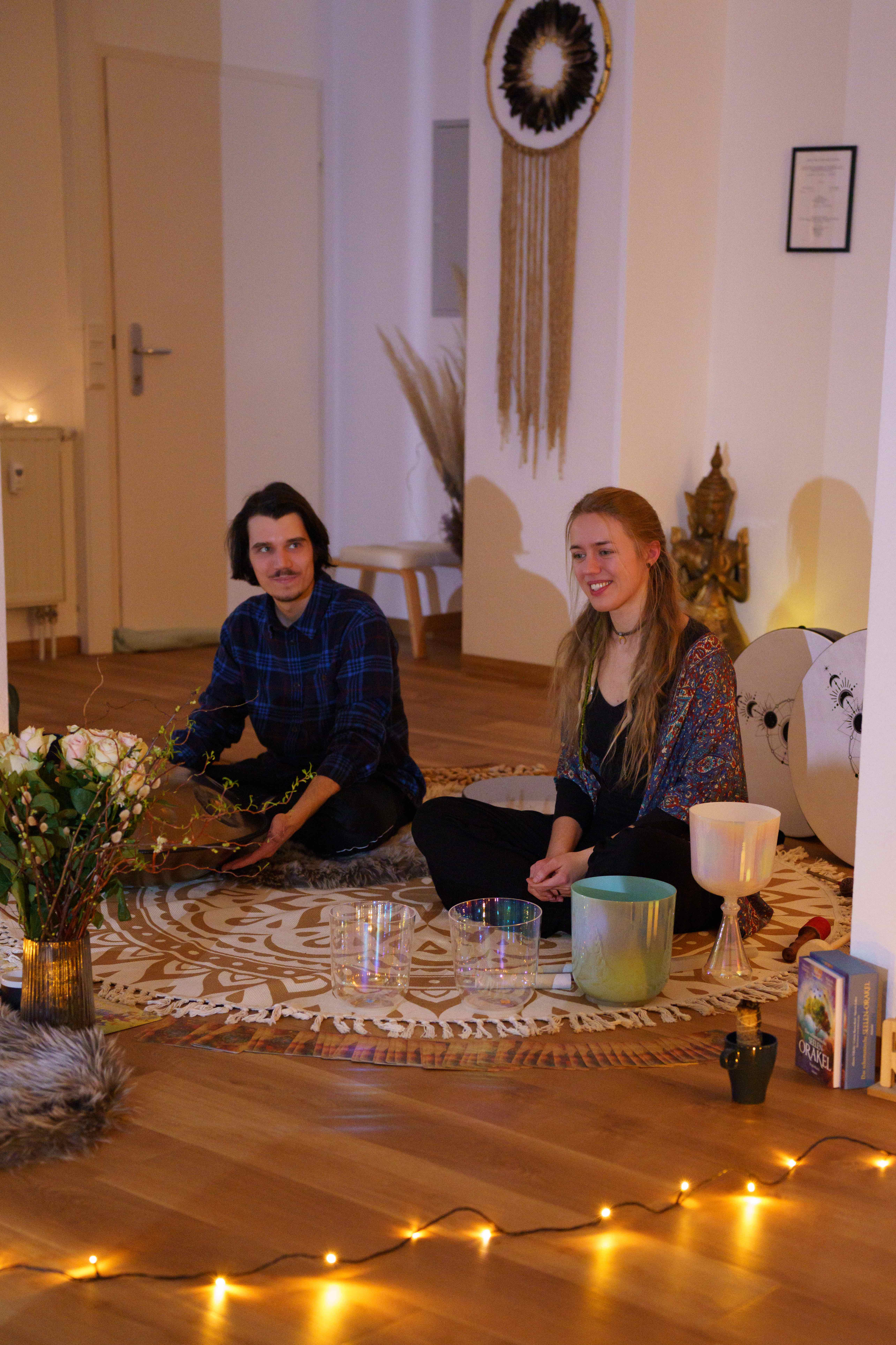 Zwei Menschen sitzen auf einem gemusterten Teppich in einem gemütlichen Raum mit sanfter Beleuchtung.