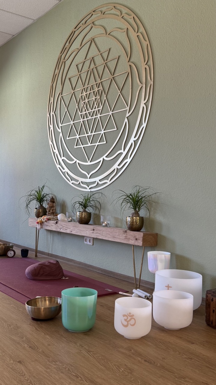 Meditationsraum mit Klangschalen, Meditationskissen, Pflanzen und Wanddekoration für Entspannung.