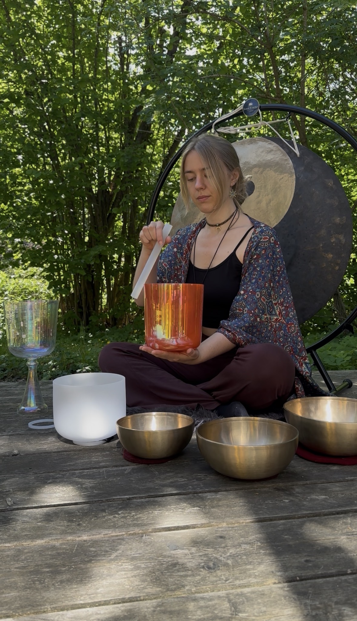 Frau sitzt im Schneidersitz im Freien und spielt auf Kristall- und Klangschalen zur Meditation.