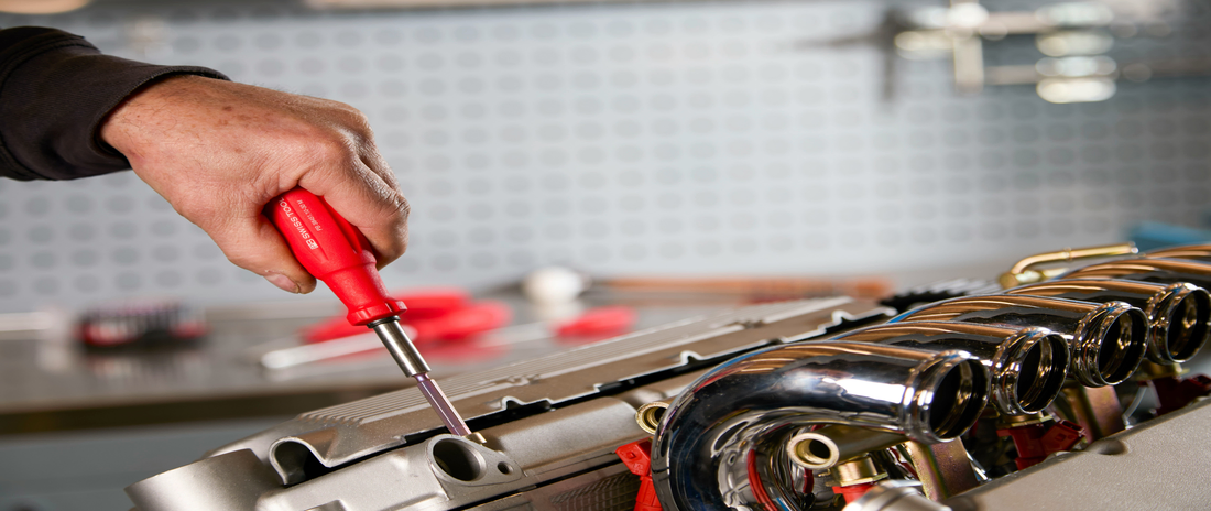 Handwerker arbeitet mit einem Schraubenzieher an einem Motorblock – Symbol für den Ort der Leistungserbringung.