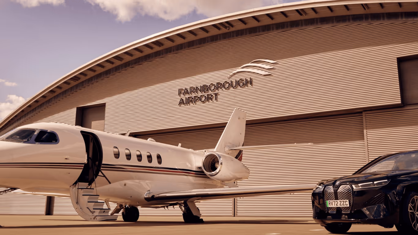Private jet with open door parked outside a hangar at Farnborough Airport next to a black luxury BMW car.