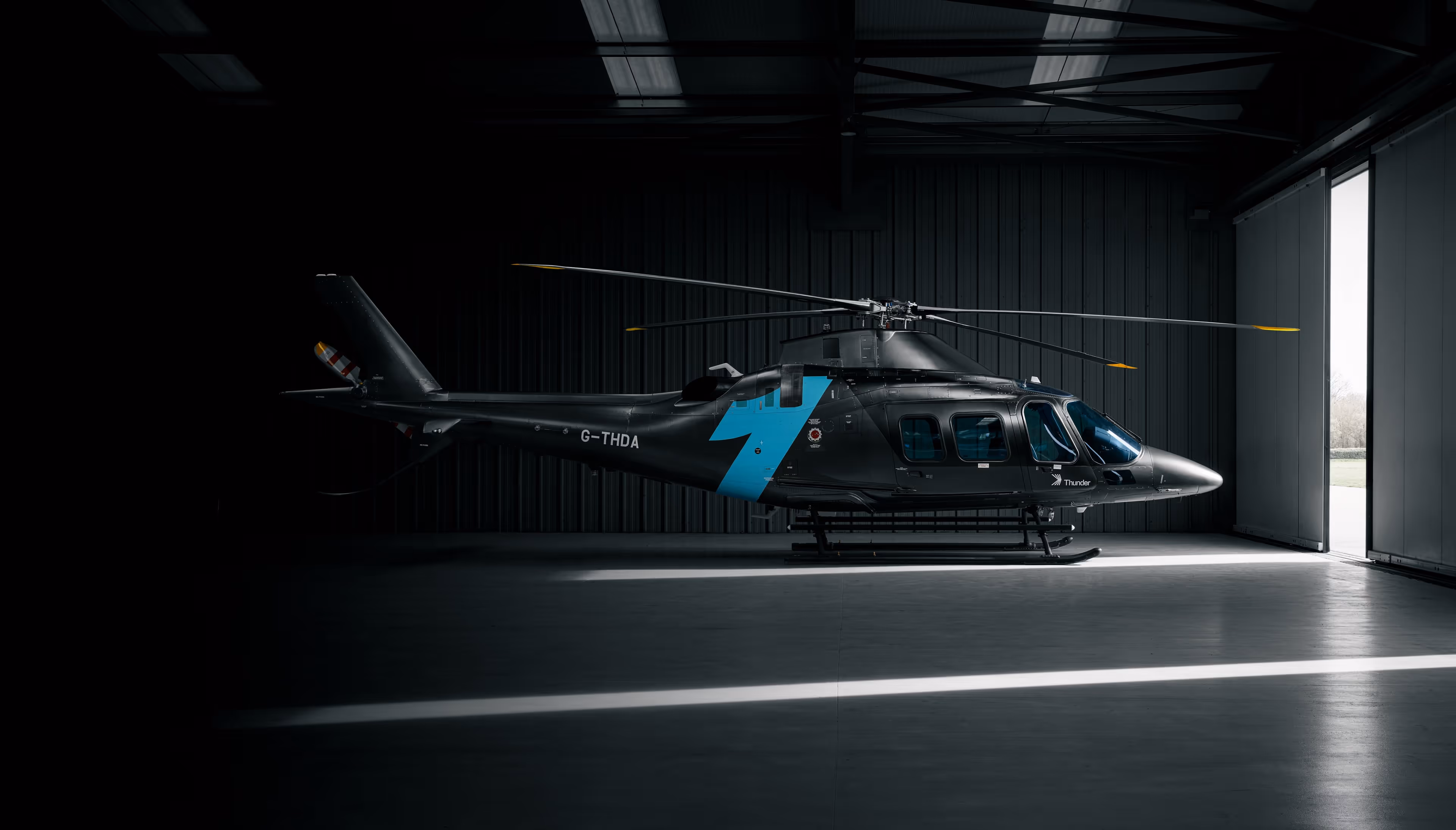 Black helicopter with blue lightning bolt parked inside a dimly lit hangar near an open door.