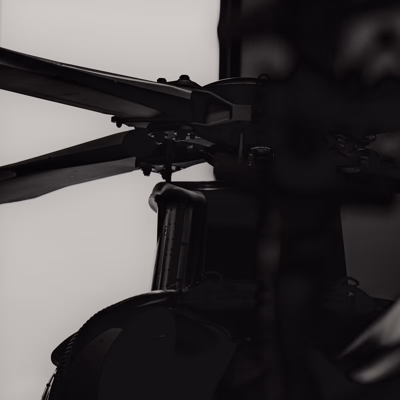 Close-up of helicopter rotor blades and hub in silhouette against a light background.
