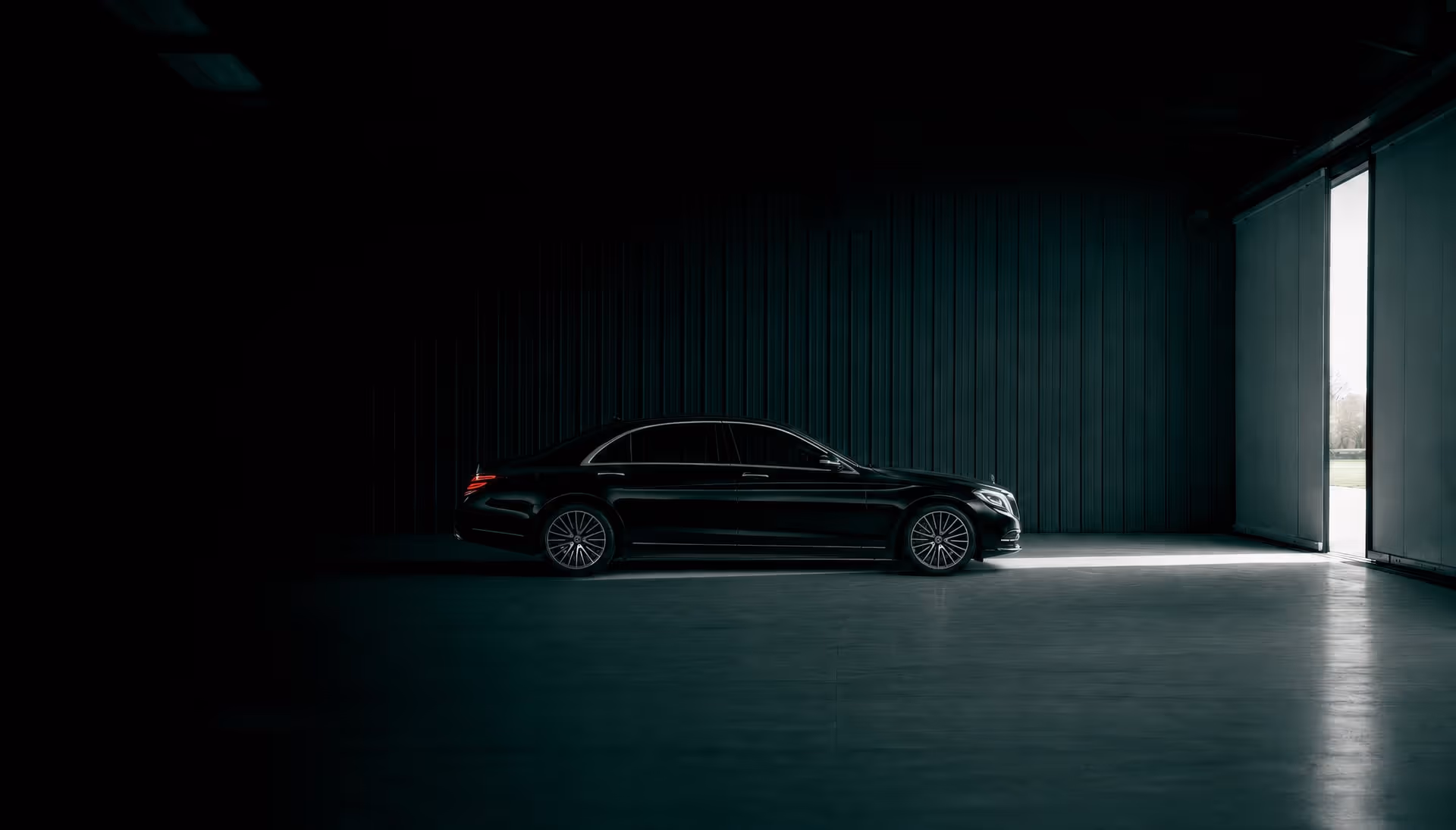 Black luxury sedan parked in a dim garage illuminated by light from an open door.
