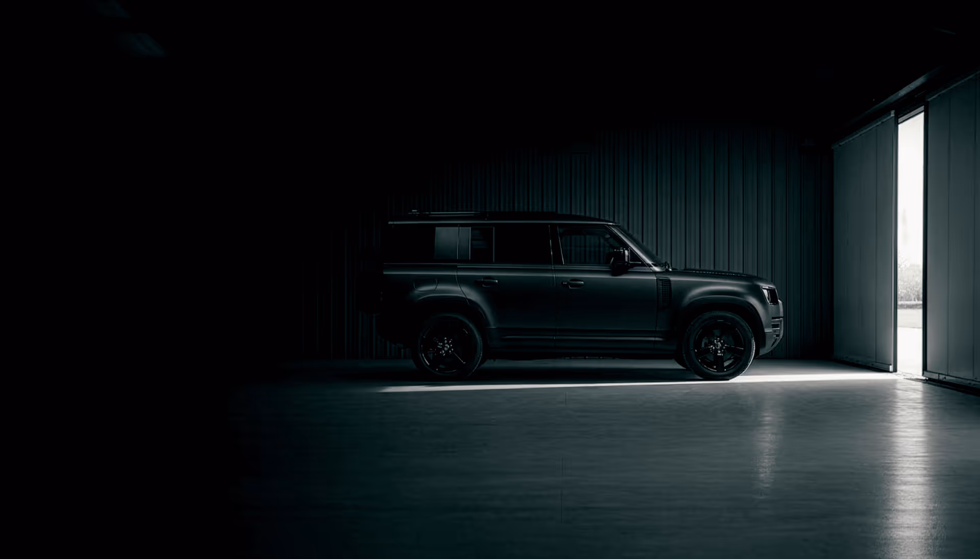 Matte black SUV parked inside a dimly lit garage with light coming through an open door.