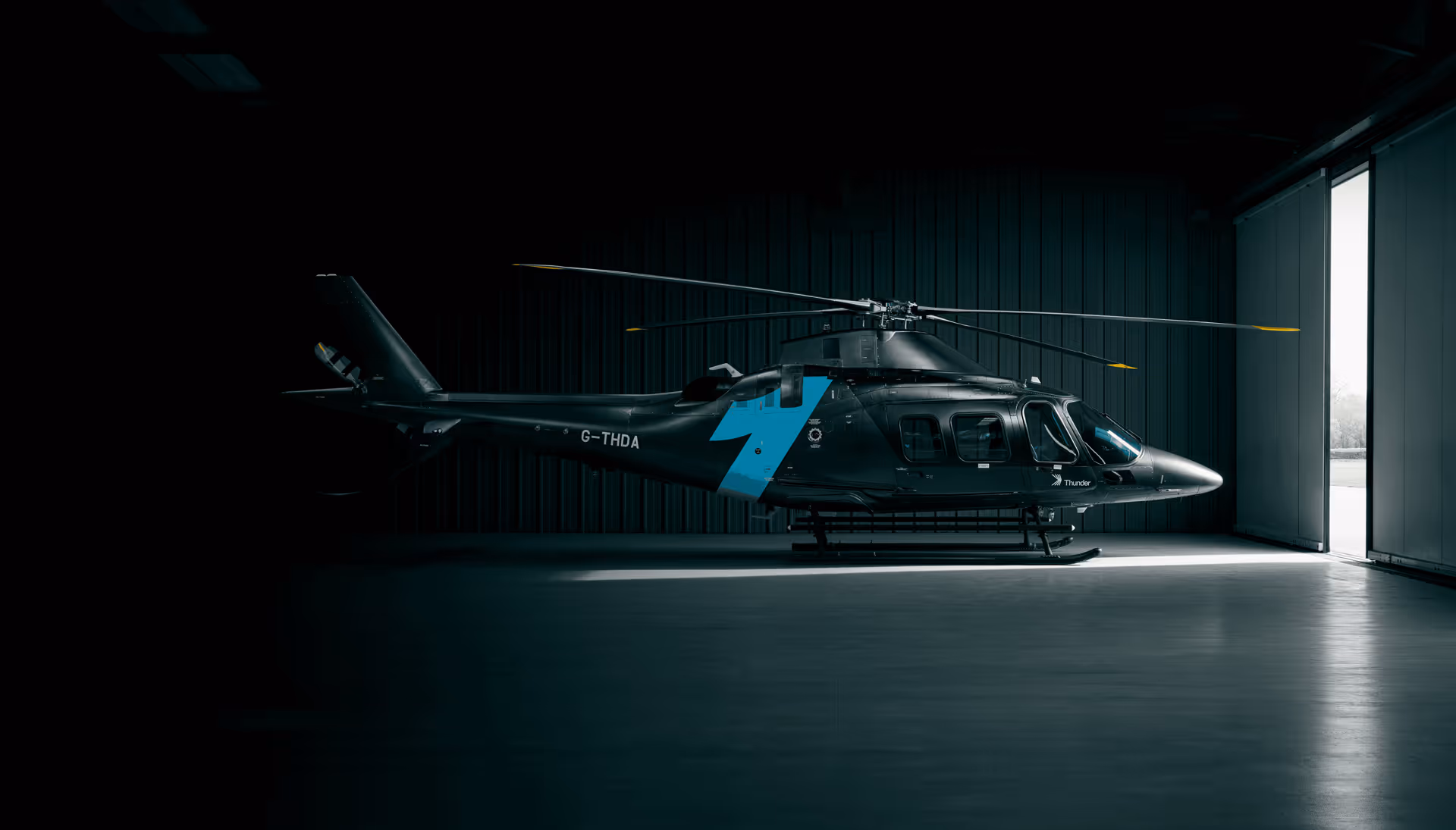 Black helicopter inside a dimly lit hangar with open doors.