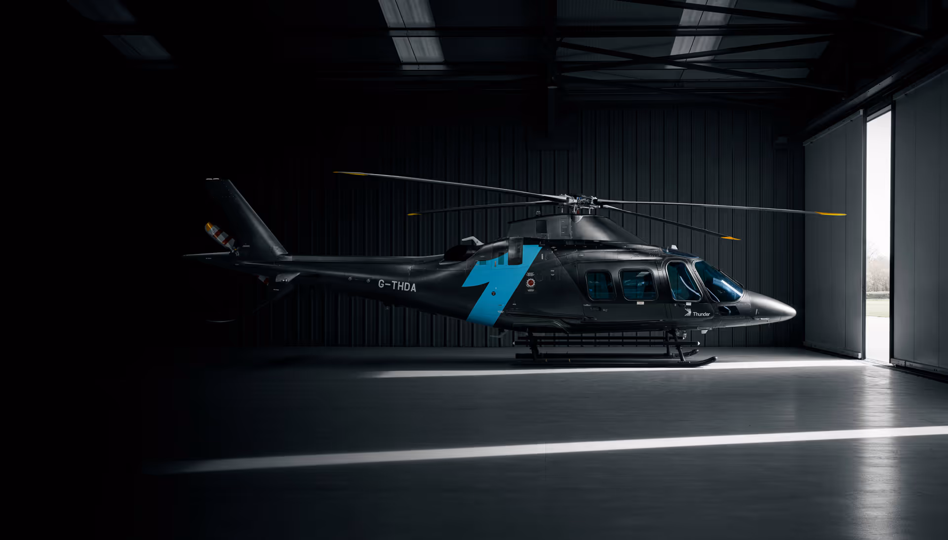 Black helicopter with blue lightning bolt decal parked inside a dimly lit hangar with open door.