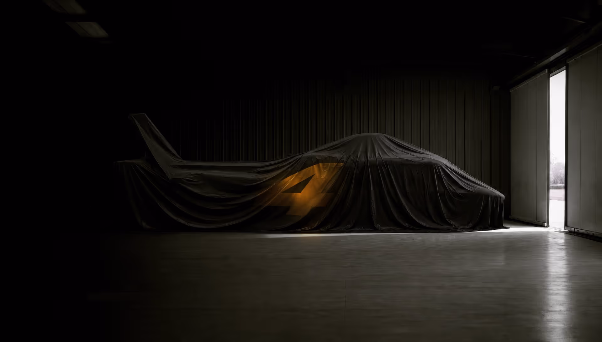 Race car covered by black sheet in dim garage, number 4 glowing softly beneath fabric.