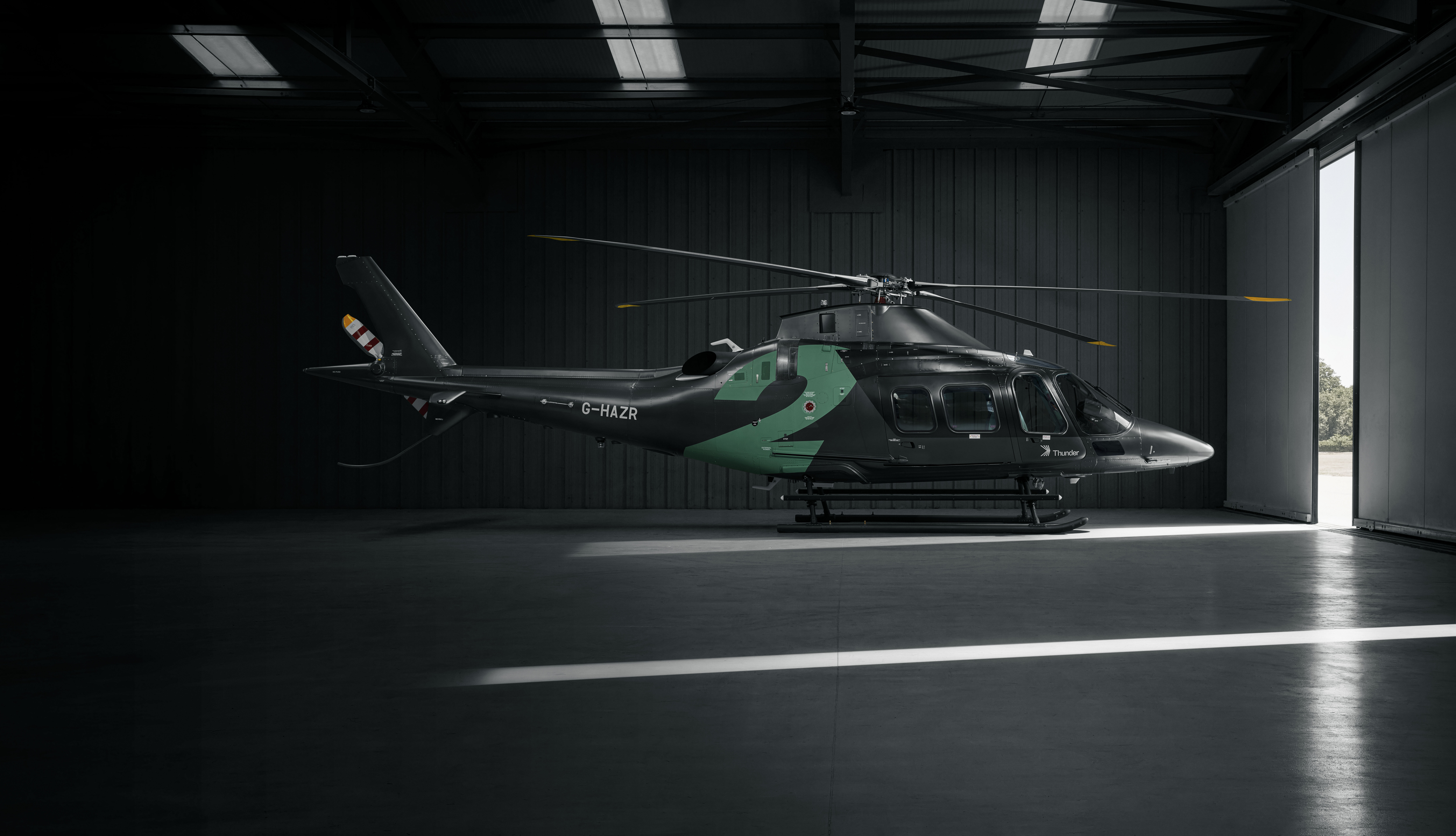 Helicopter covered with a dark cloth showing a glowing number 2 in a dim garage by an open door.