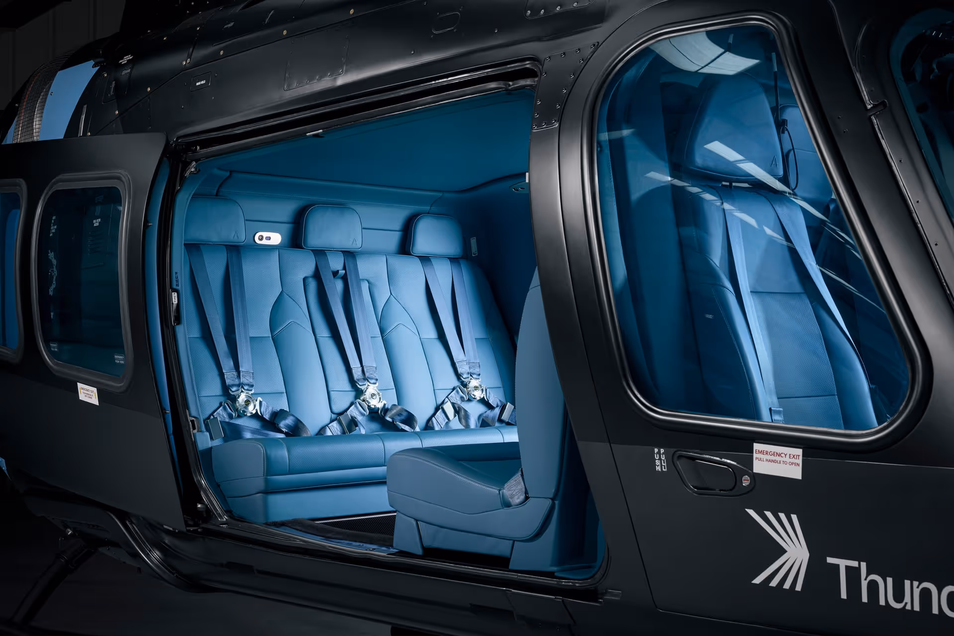 Open helicopter door showing modern blue leather seats with safety harnesses inside.