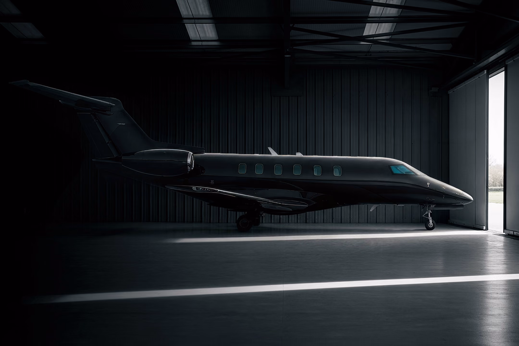 Black private jet parked inside a dimly lit hangar with open hangar doors.