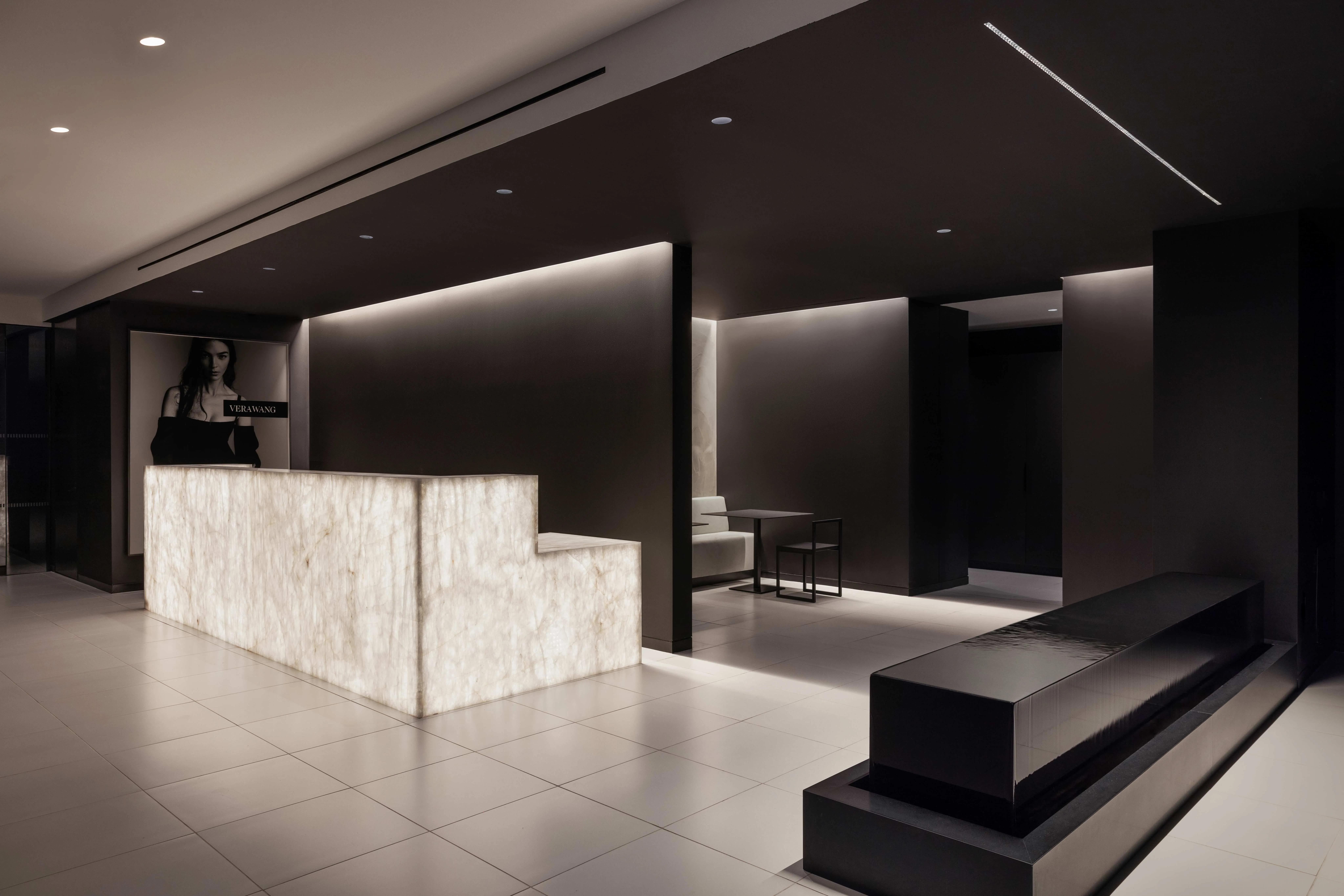 Spectorgroup-designed Vera Wang headquarters reception with backlit onyx desk, dark walls, and brand campaign imagery