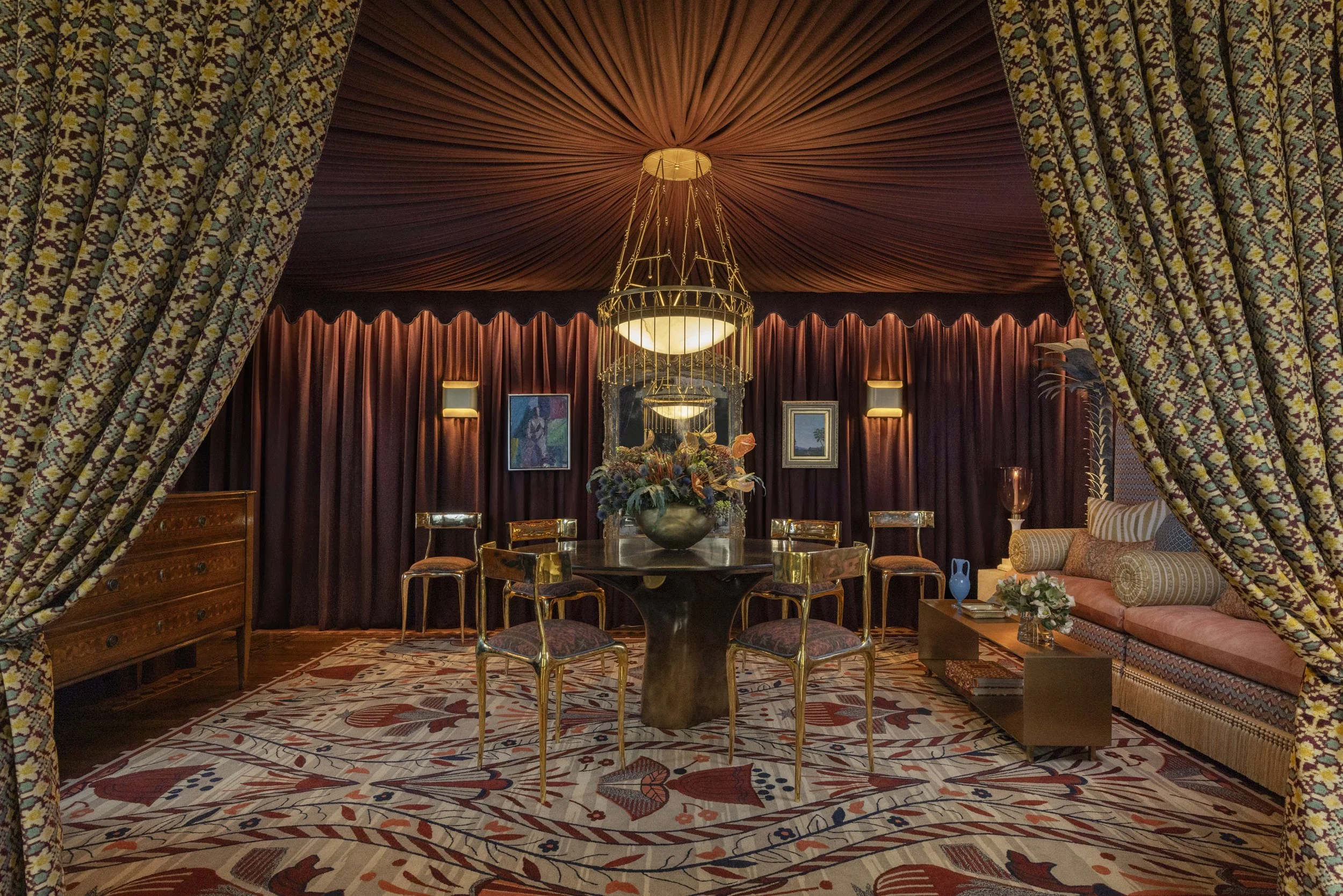 Sen Creative maximalist dining room with draped tent ceiling, brass chandelier, patterned rug, and floral print curtains