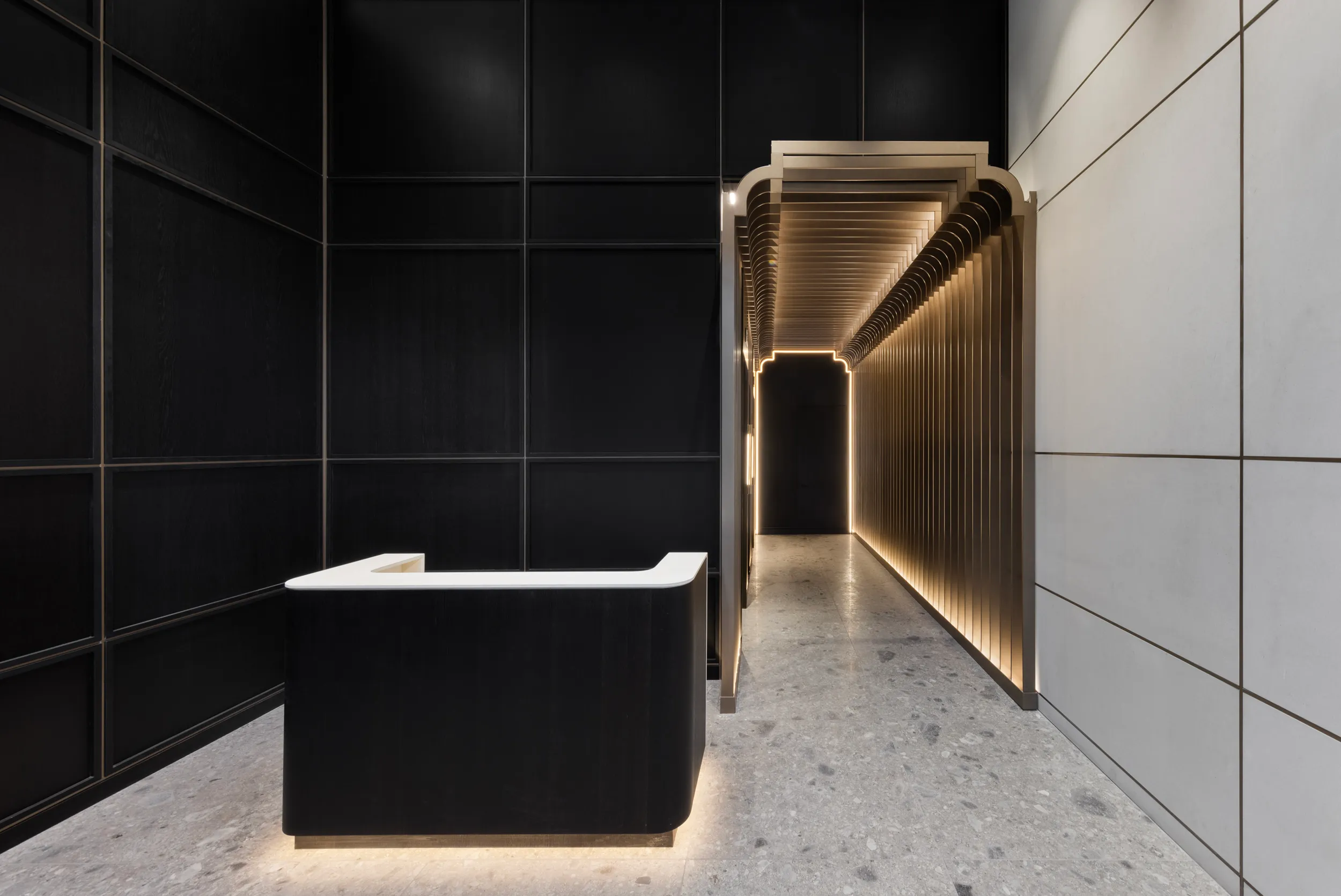 Spectorgroup designed 836 Broadway retail reception with black panel walls, white desk, and illuminated bronze arch corridor