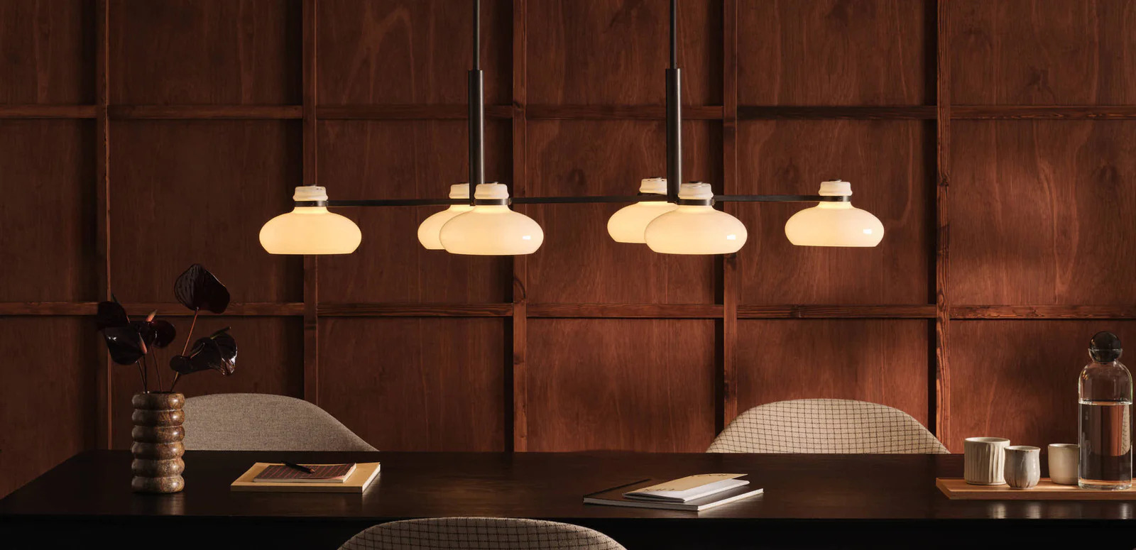 Original BTC Magnus pendant lights with opal glass shades suspended over a dark wood dining table against warm wood paneling
