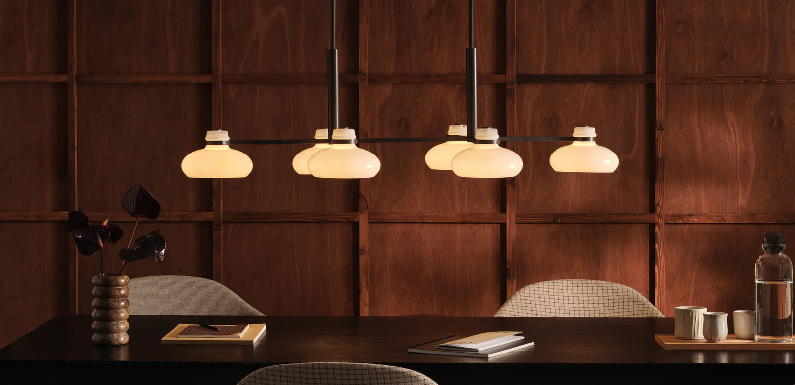Original BTC Magnus pendant lights with opal glass shades suspended over a dark wood dining table against warm wood paneling