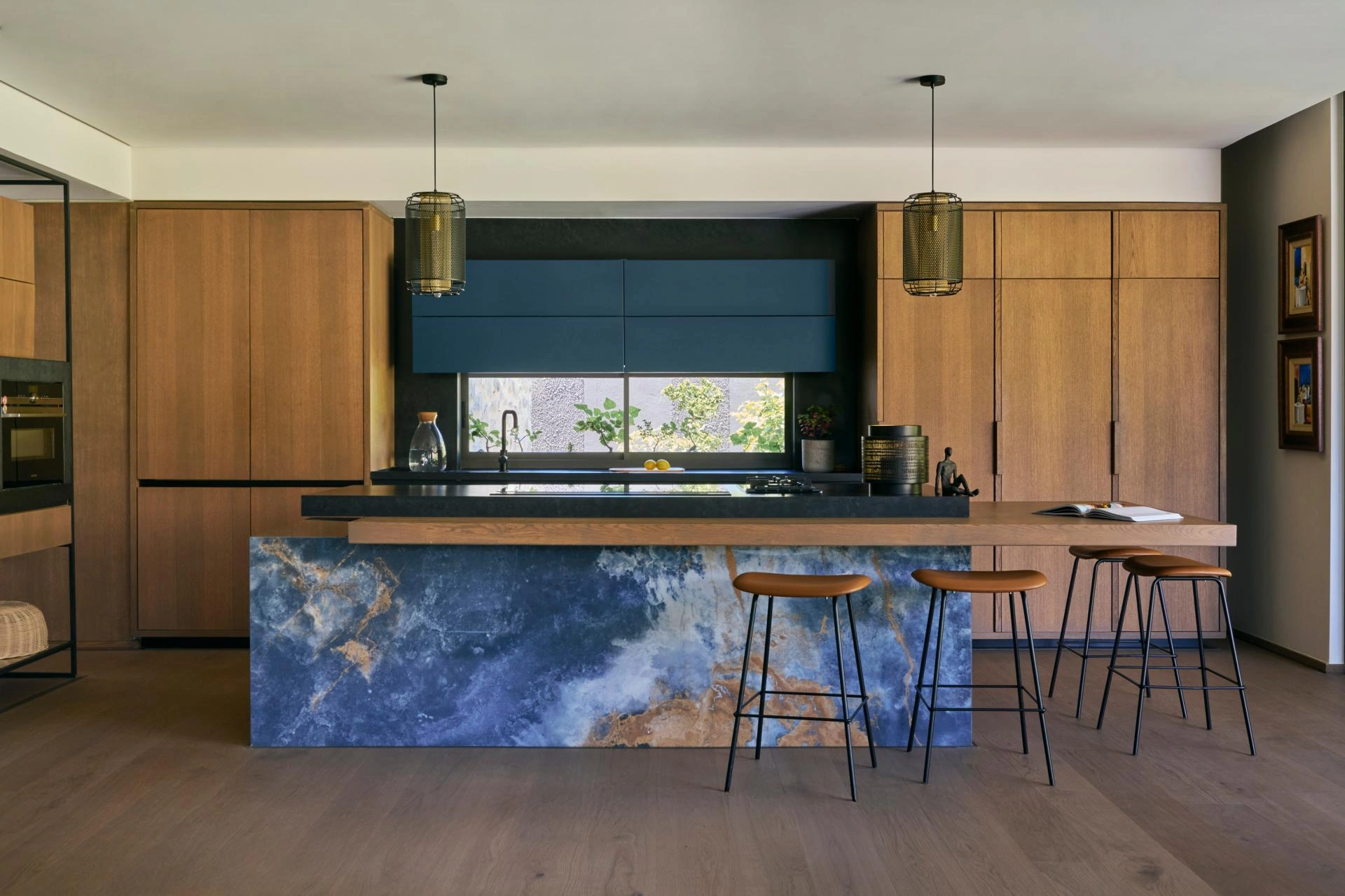 Bjelin wood flooring in a modern kitchen with bold blue stone island waterfall, walnut cabinetry, and leather bar stools