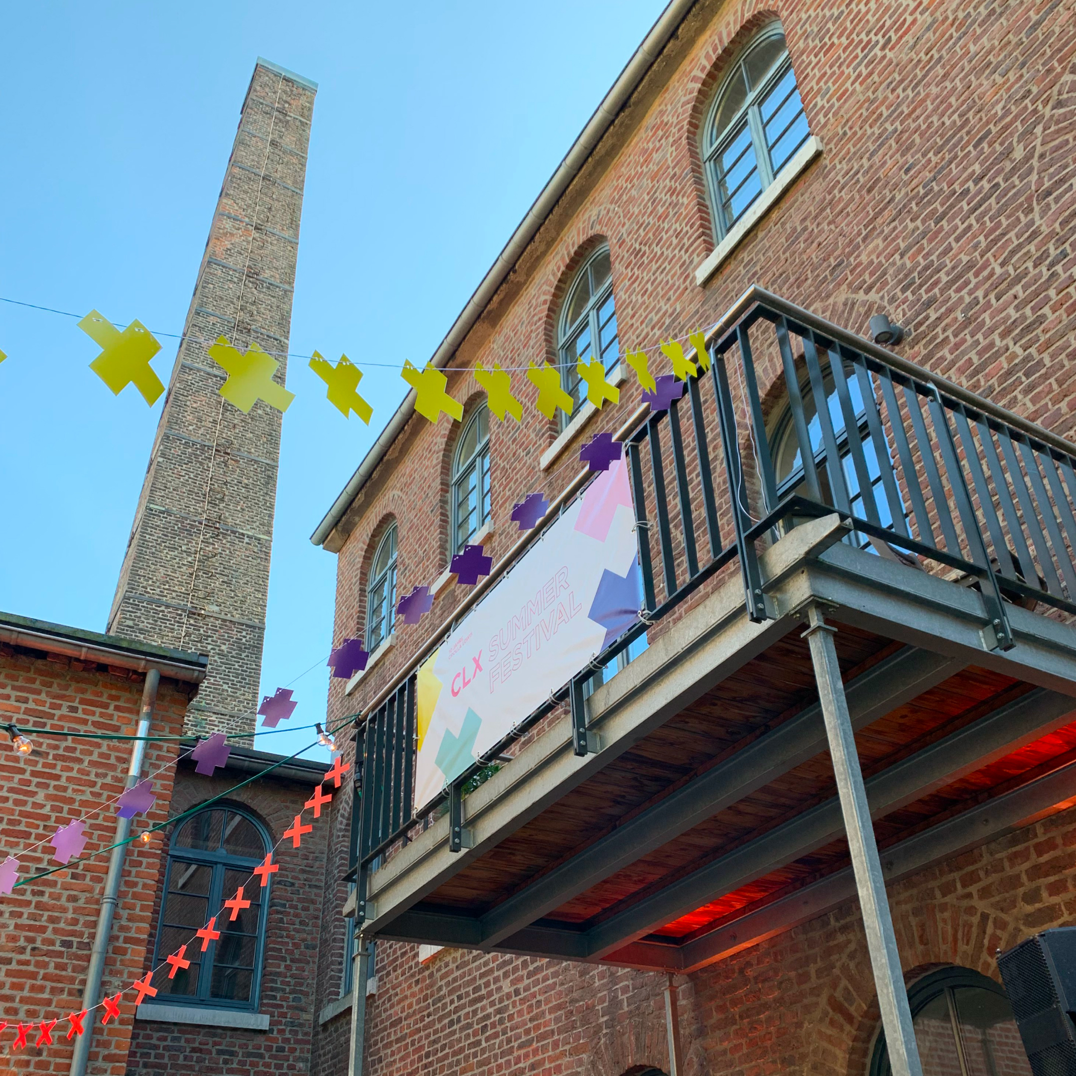 Backsteingebäude mit Balkon, bunten Girlanden und Banner für CLX Summer Festival bei blauem Himmel.