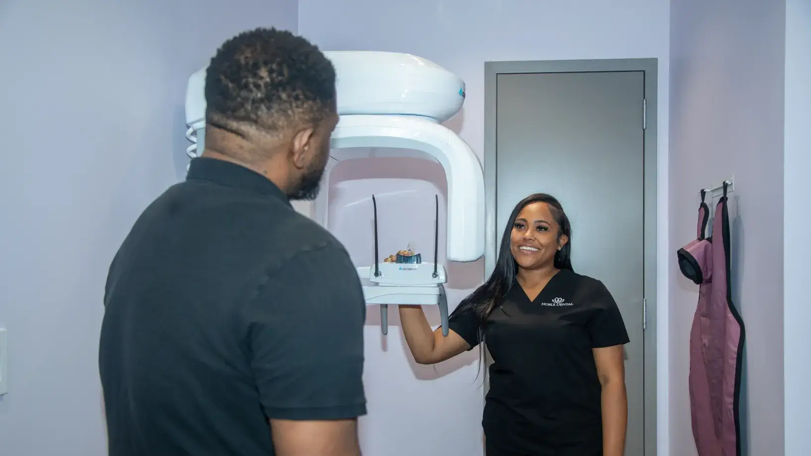 A dental technician positions a patient for an X-ray in a dental office.