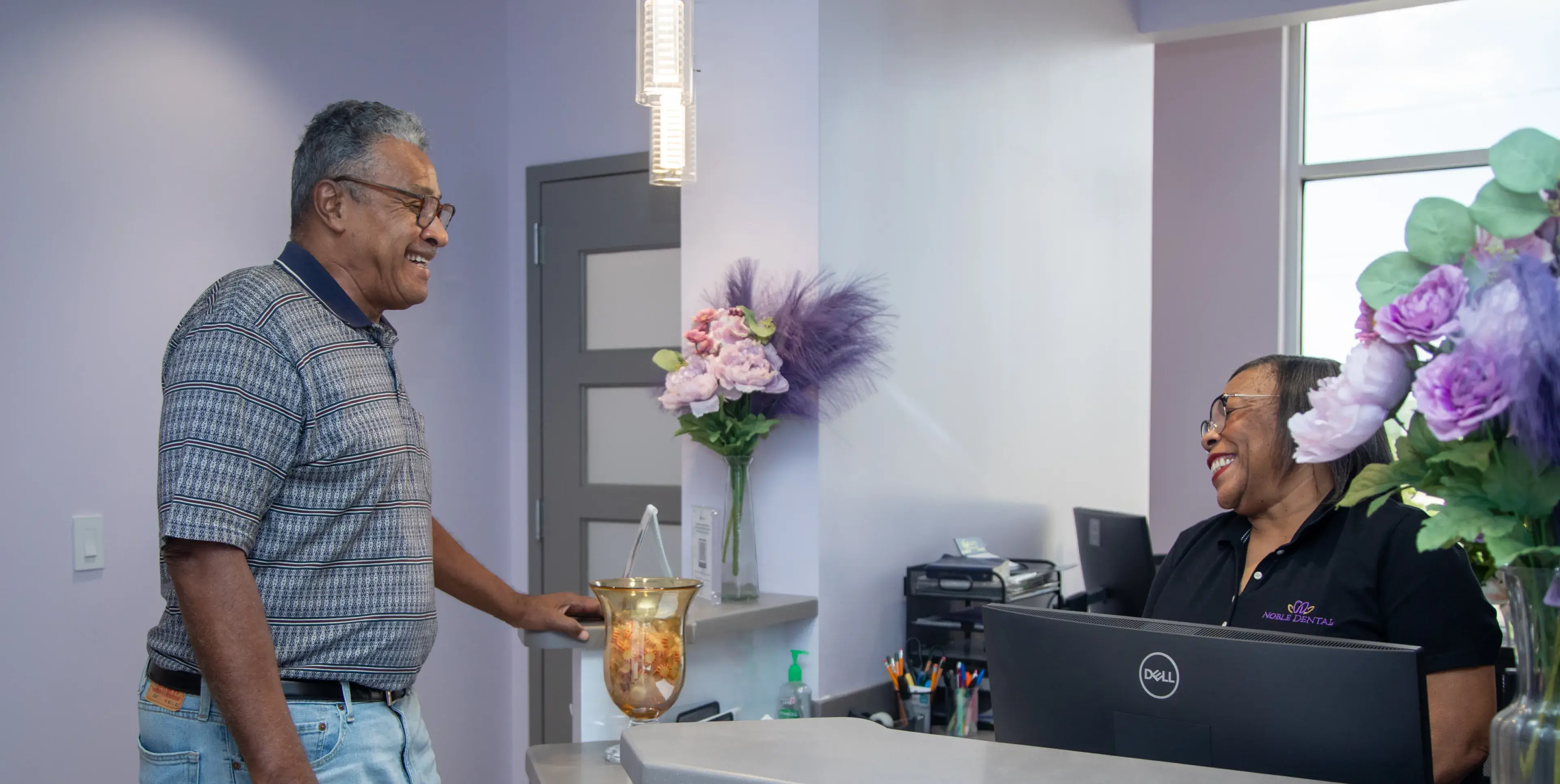 Man smiling while talking to a woman seated at a reception desk.