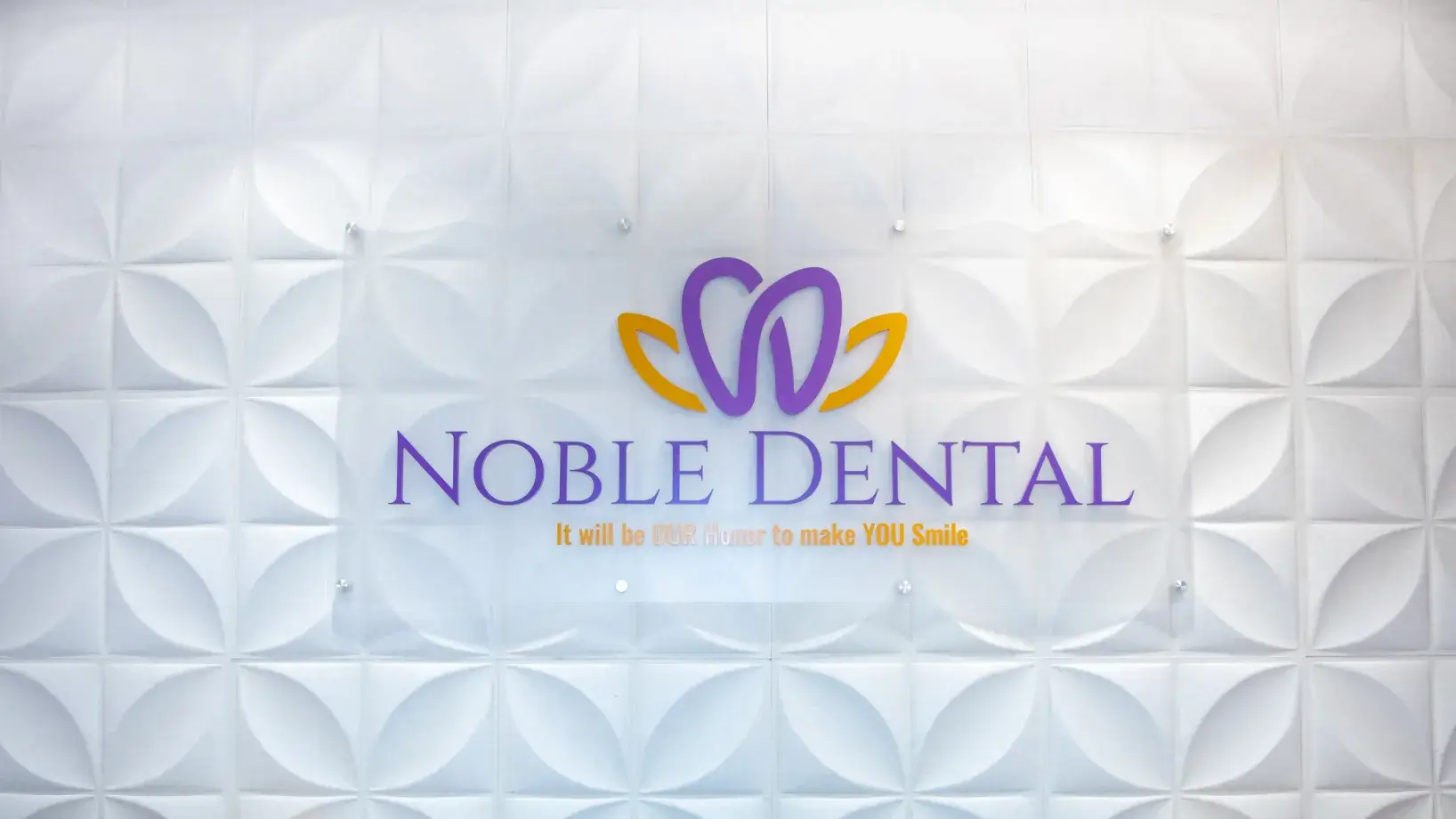 Sign that reads "Noble Dental: It will be our honor to make you smile" on a patterned wall.