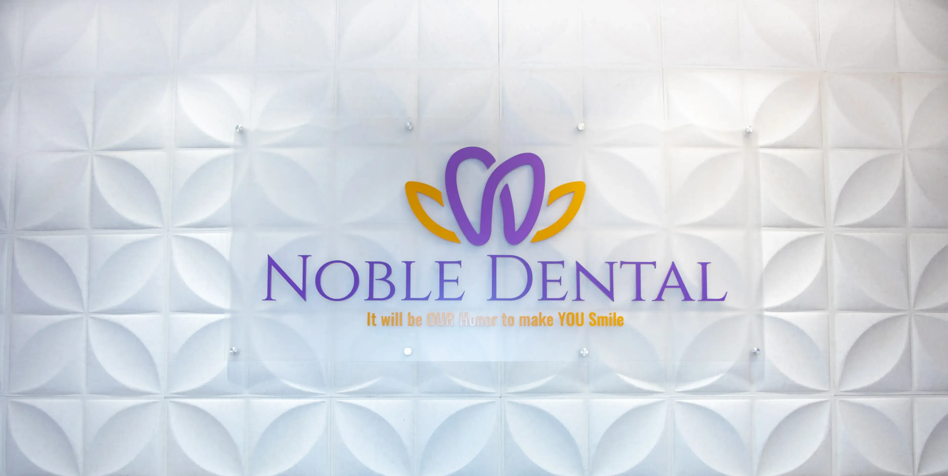 Noble Dental logo on a textured wall, featuring purple and yellow design elements.