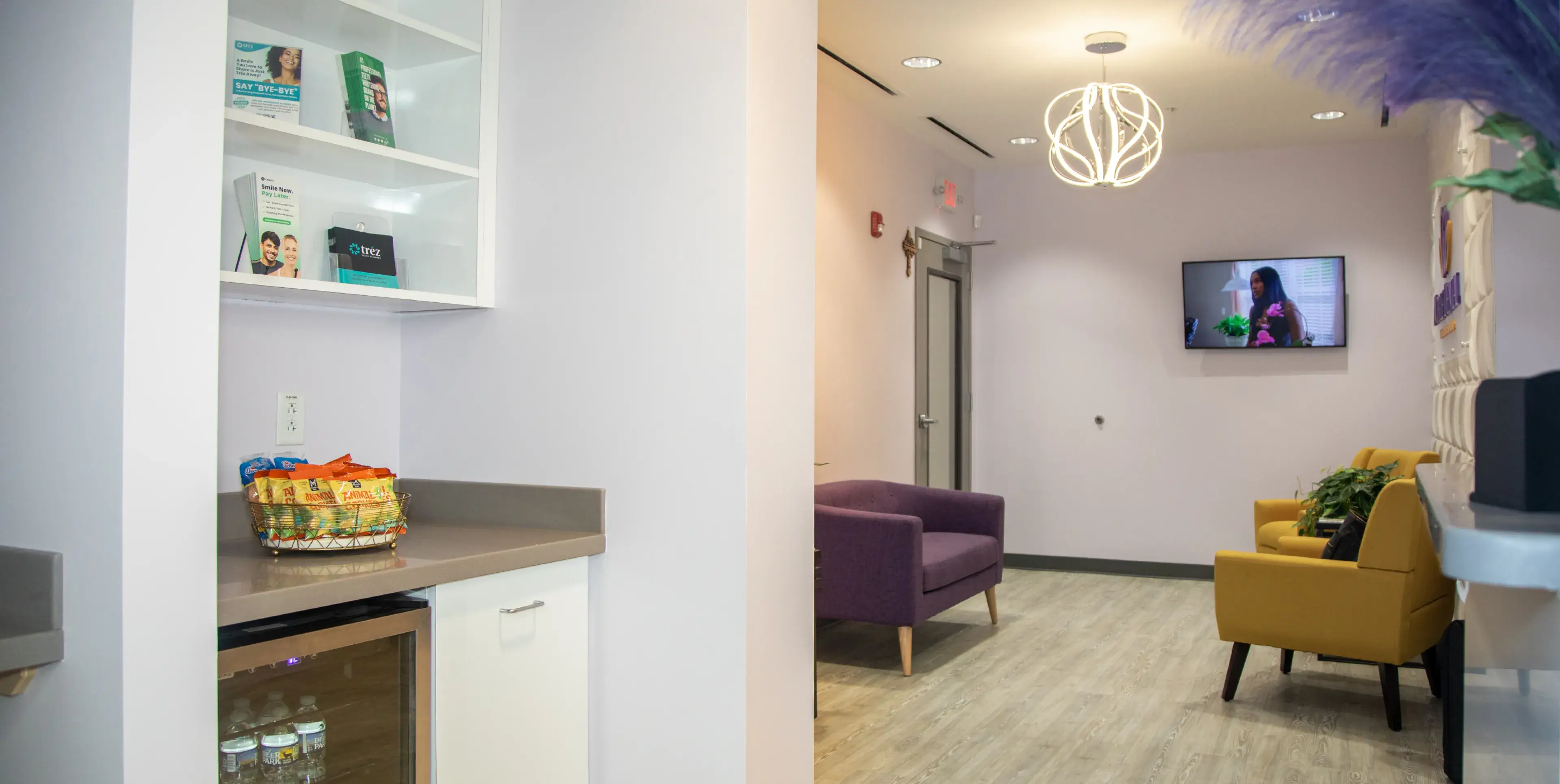 A waiting room with purple and yellow chairs and a TV showing a person talking.