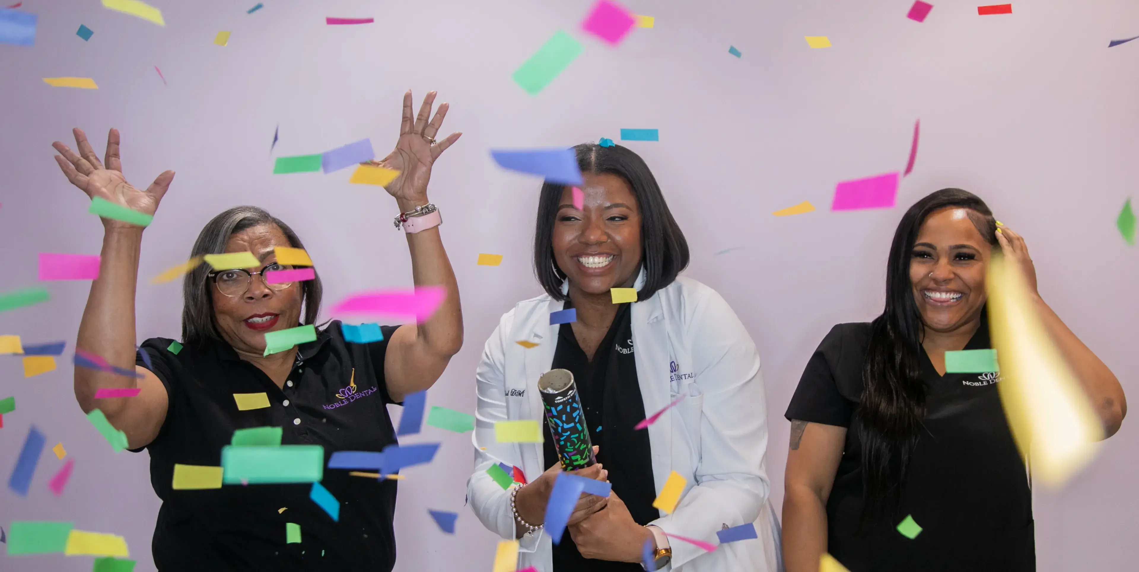Three women celebrate joyfully with colorful confetti falling around them.