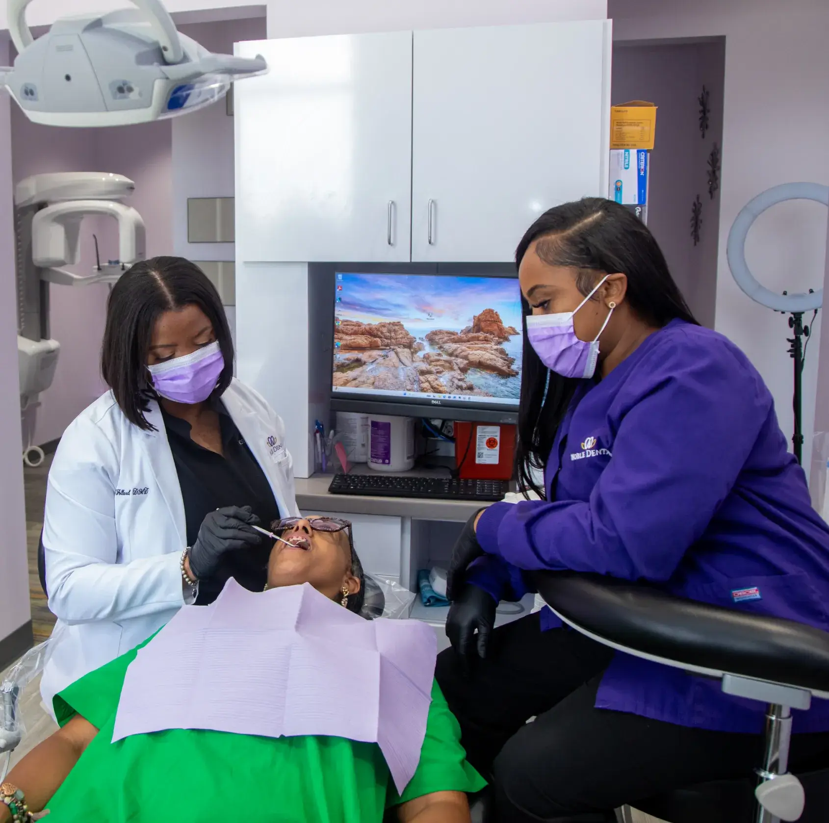 Two dental professionals in masks examine a patient's teeth in a dental office.