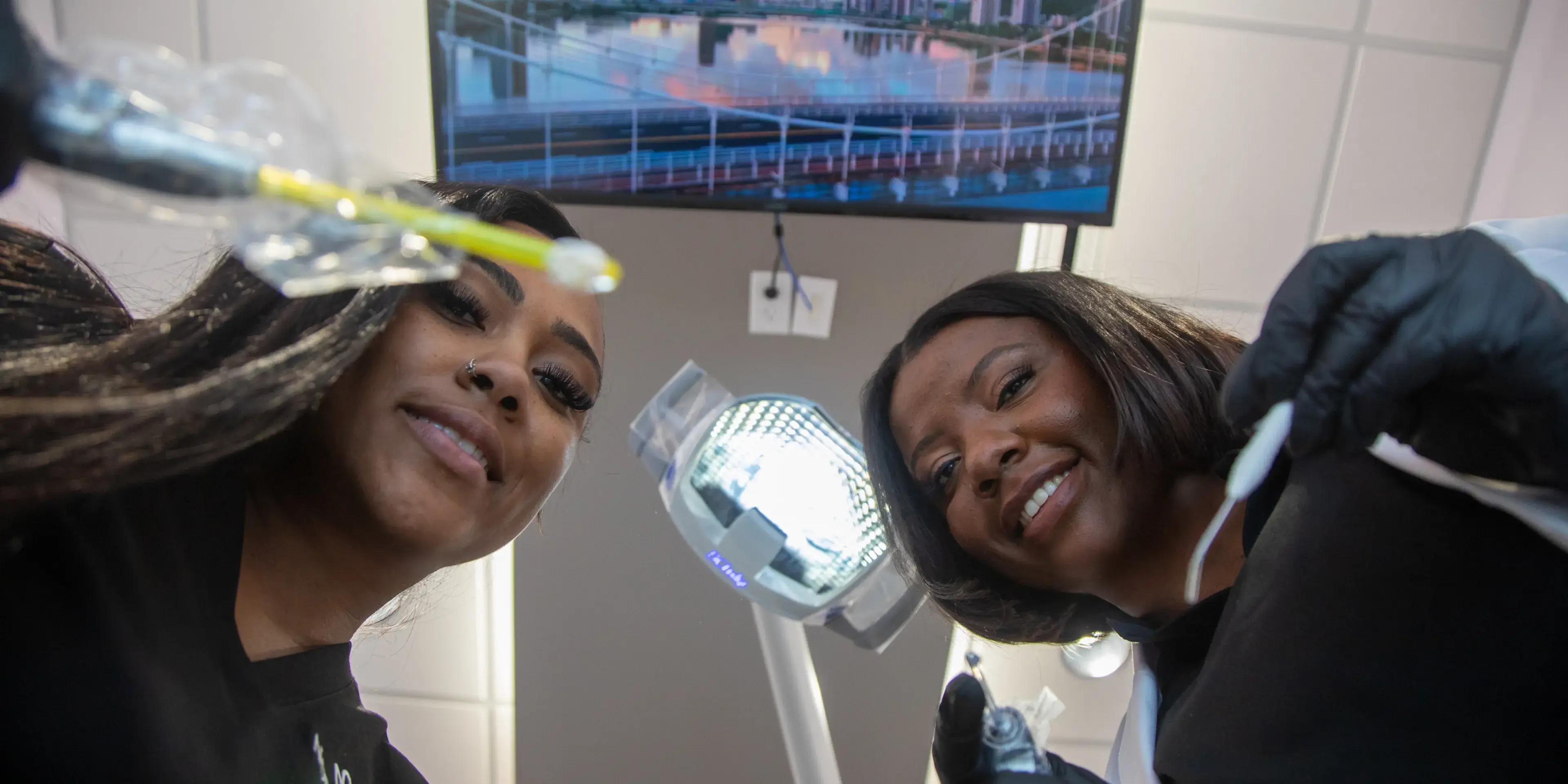 Two dentists, wearing gloves, look down at the camera while holding dental tools.